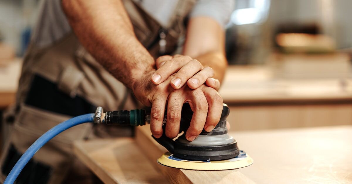 Man using sanding tool on piece of hardwood